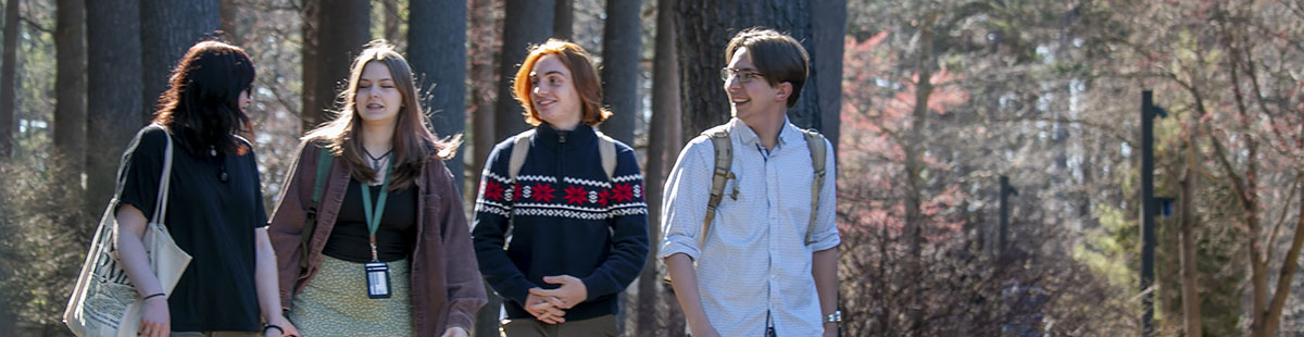 Four NMC students walking by the pines near the Osterlin Building